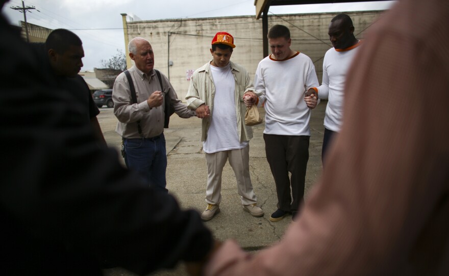 Bill Kleiber, director of Restorative Justice Ministries, in suspenders, leads a circle of released inmates in a prayer shortly before they board a bus.