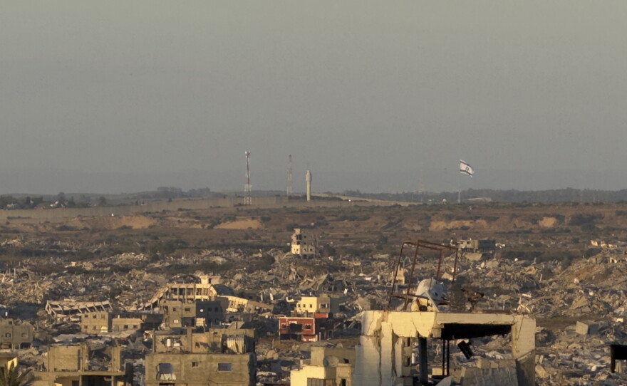 A large Israeli flag waves in the distance over a landscape of destruction and debris in Gaza near the border with Israel.
