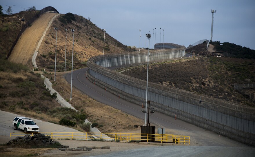 A section of secondary fencing, covered with concertina wire at the base and top of the structure, snakes along a winding road near the San Ysidro Port of Entry in San Diego on Aug. 16, 2017. Also shown is a line of primary fencing made of corrugated steel, left, a Border Patrol vehicle along a drainage area and a tower with “virtual fencing” technology at the top of the hill.