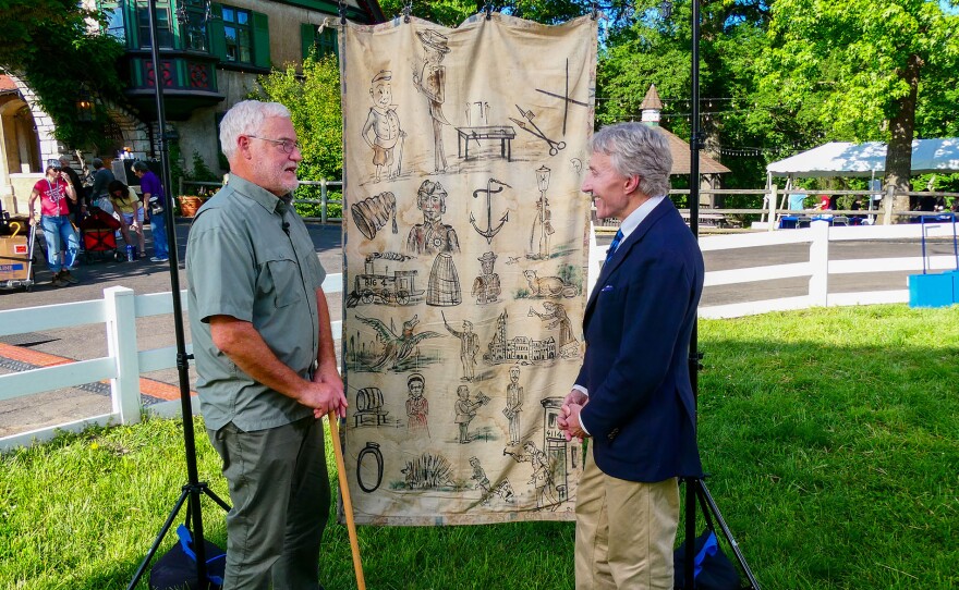 Leigh Keno (right) appraises 1904 painted mnemonic banner for Schnitzelbank song in St. Louis, Mo. ANTIQUES ROADSHOW “Grant’s Farm, Hour 1” premieres Monday, April 27 at 8/7C PM on PBS.