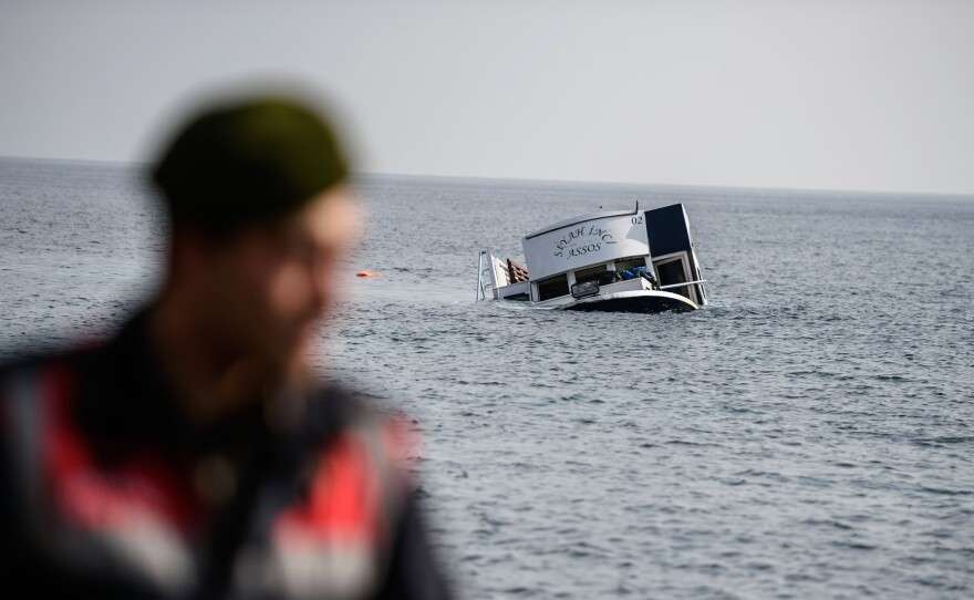 A sinking boat is seen behind a Turkish gendarme off the coast of Canakkale's Bademli district on Saturday. At least 35 migrants drowned when their boat sank in the Aegean Sea while trying to cross from Turkey to Greece.