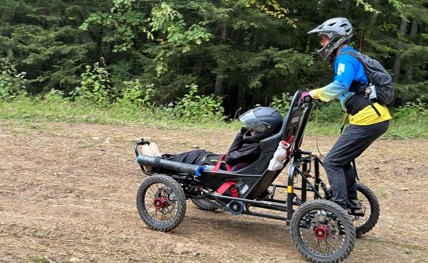Carol Woody steers the Cimgo while standing firmly on the foot pegs at the back of the all-terrain device. Gage Tatar rides in the Cimgo giggling and smiling his way down the dirt path at Snowshoe Resort.