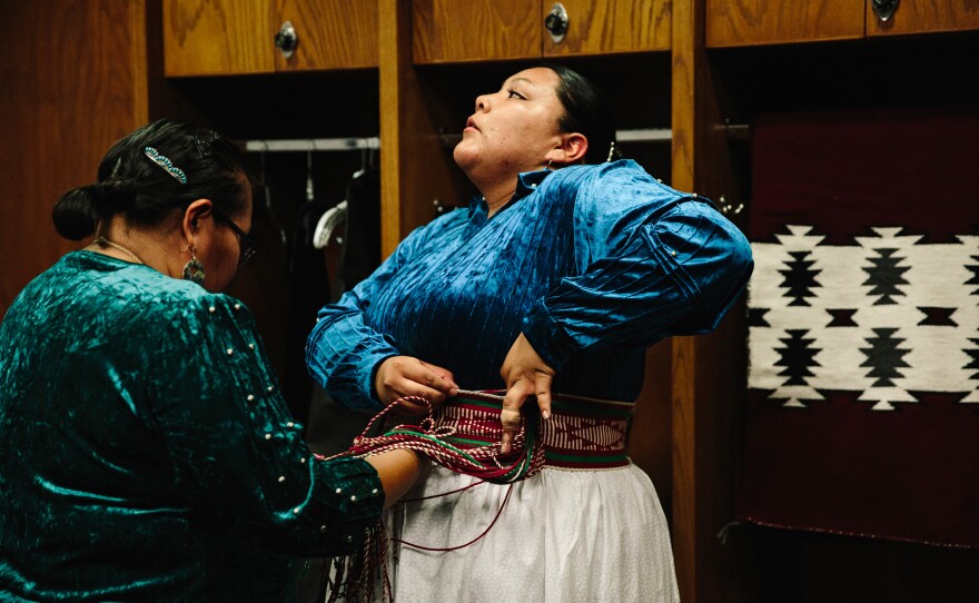 Montoya tightens her sash belt with the help of Miss Navajo Nation adviser Roberta Diswood in the women's locker room.