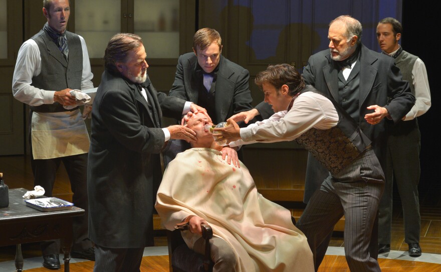 The actor playing William Morton administers ether via a glass tube to a patient about to have a tumor removed. It's the first successful demonstration of anesthesia in a hospital setting.