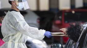 A health worker gives out rapid COVID-19 antigen self-test kits at the Waipareira Trust drive-in COVID-19 testing station in Auckland, New Zealand, on Tuesday.