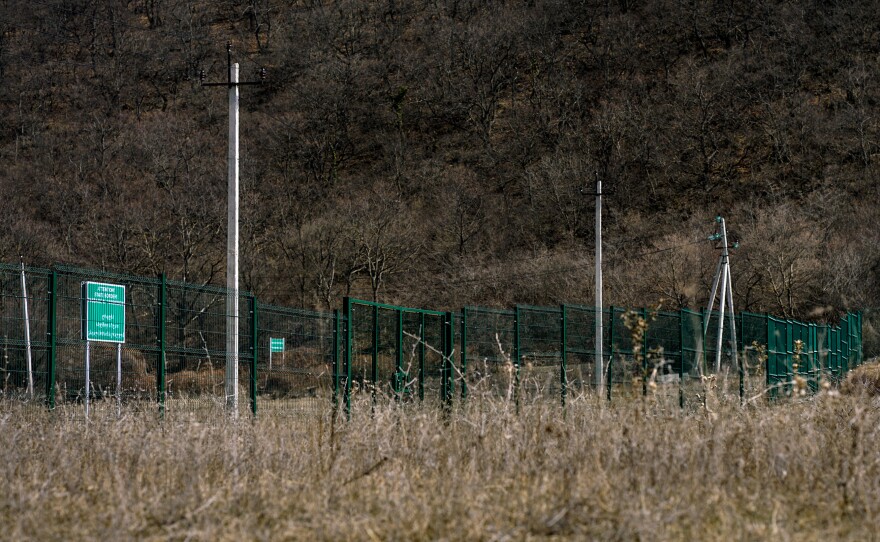 A fence runs through a field that outlines the de facto border between Georgia (right) and Russian-controlled South Ossetia (left). The sign says, "Attention! State Border! Passage Is Forbidden!"