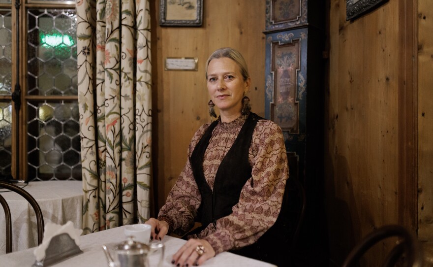 Servane Giol, renowned expert in Venetian art and lifestyle, poses in the historic wood-paneled Stube of the Hotel de la Poste. Giol, who has dedicated her work to preserving the cultural and aesthetic heritage of the region, sits beside an old painted pendulum clock, a symbol of the hospitality and Ampezzo tradition that the hotel has represented since 1804.