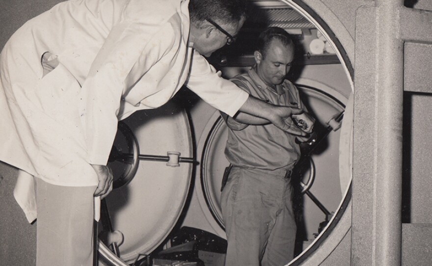 George Bond assists Bob Barth from the entrance way to the Genesis E chamber, 1963.