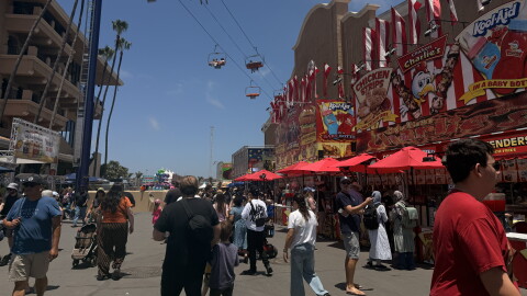 Visitors walk down a food-vendor lined walkway as the gondola ride passes overhead at the San Diego County Fair on June 10, 2026.