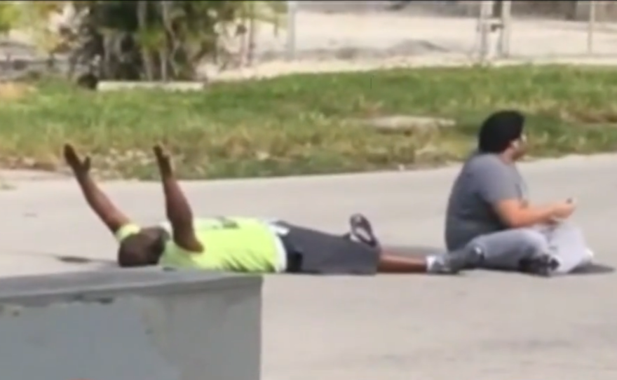 In a video filmed on Monday, Charles Kinsey (left) lies next to the autistic patient he was trying to help, holding his hands up in an effort to assure the North Miami police that they weren't a threat. Kinsey was later shot in the leg by the police.