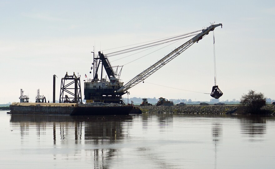 A dredge drops rocks onto a damaged levee in California's delta.