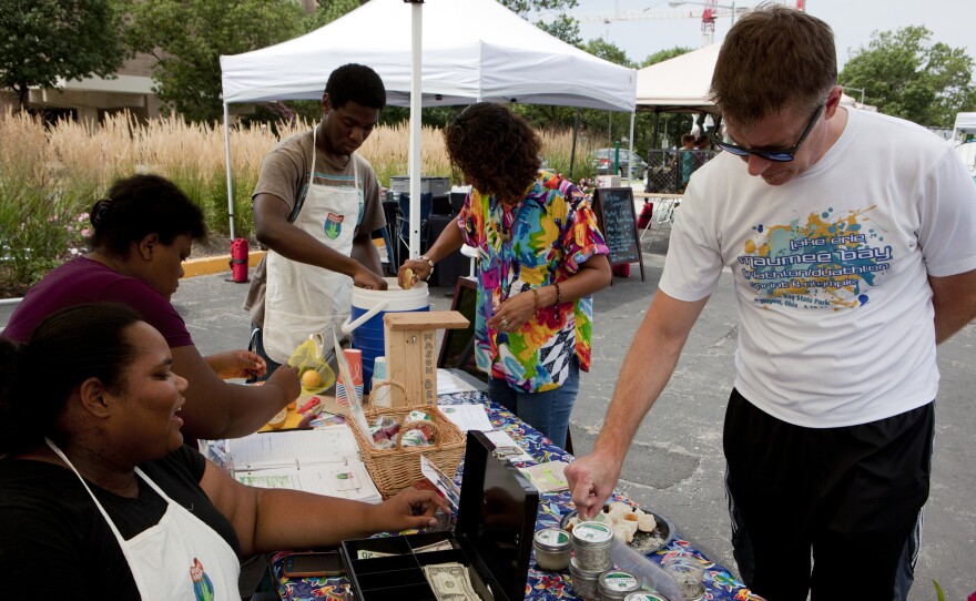 Roshawn Little (left), invites customer Nate Kohring to try the herbed salt with bread at the Aya Farmers Market on Saturday.