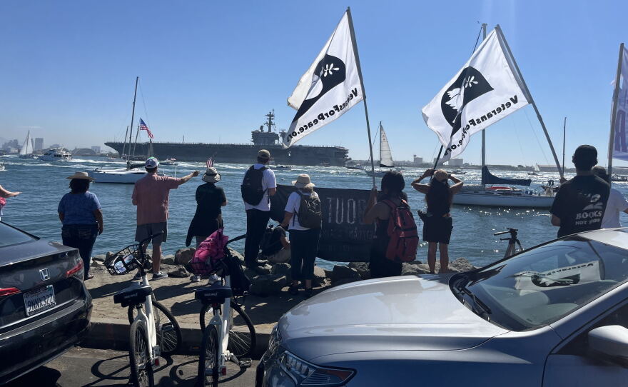 Supporters and protestors gather with signage along Shelter Island's shoreline for the USS Lincoln's arrival, Oct. 8, 2026.