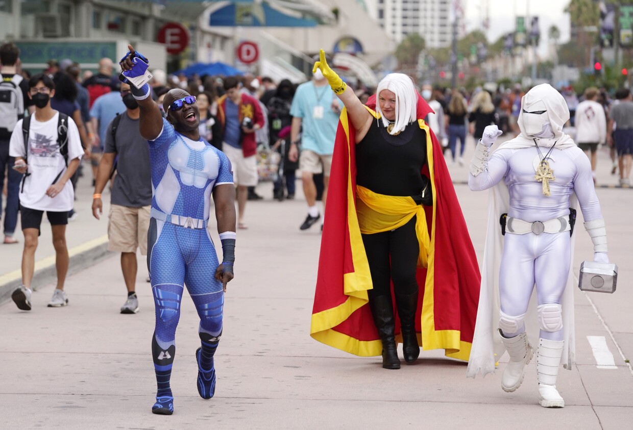 Jay Acey, left, dressed as A-Train from the television series "The Boys," Faeren Adams, center, dressed as Marvel superhero Doctor Strange, and Derek Shackleton, dressed as Marvel superhero Moon Knight, walk together outside Preview Night at the 2022 Comic-Con International at the San Diego Convention Center, Wednesday, July 20, 2022, in San Diego. 