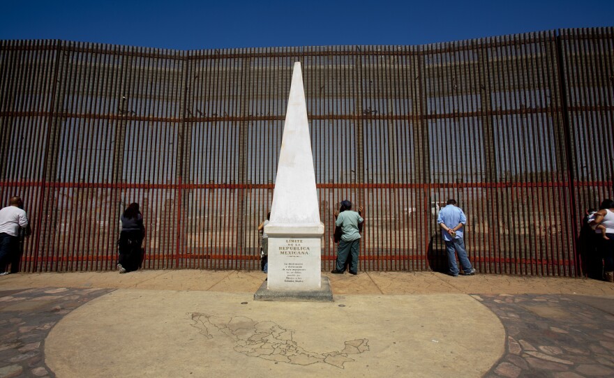 Family members huddle at the fence to talk to loved ones living across the border.