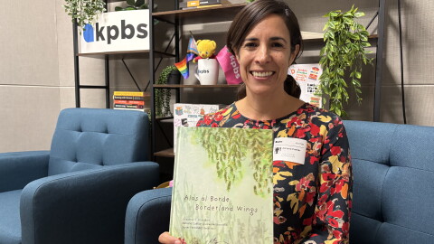 University of San Diego professor and founder of the Border Design Lab, Adriana Cuéllar, holds up her book, "Alas al Borde: Borderland Wings" in the KPBS social media studio, July 30, 2026.