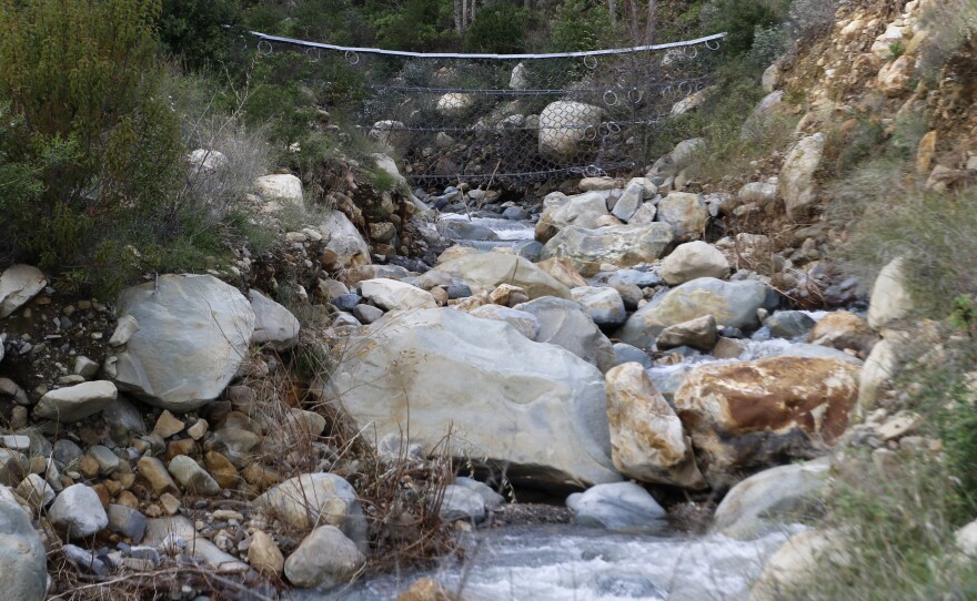 Netting made from metal cables is visible above a creek in Montecito, Calif., on Jan. 12, 2023. With climate change predicted to produce more severe weather, officials are scrambling to put in basins, nets and improve predictions of where landslides might occur to keep homes and people safe.