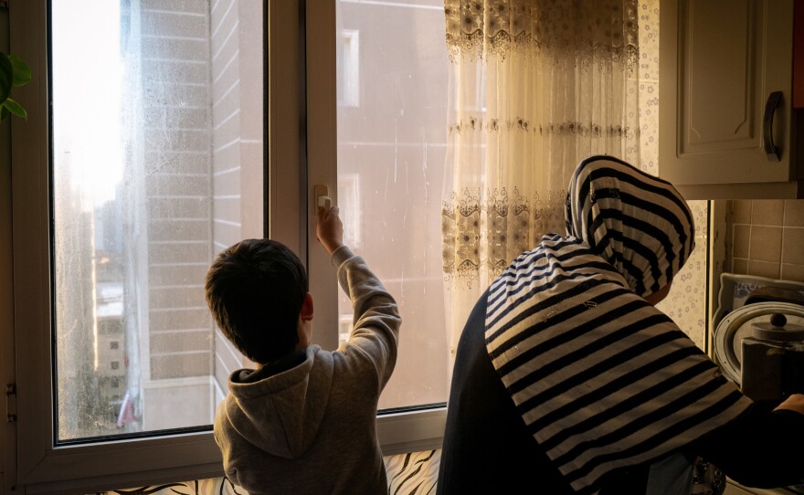 Lütfullah stands behind his stepmother, Neriman Kuçar, in their kitchen in Istanbul. She made the children <em>laghman</em>, Uyghur-style noodles, and Aysu cried. She was served Uyghur food only twice while she was at the state boarding school, but both times older classmates ate it all before she could take a bite.