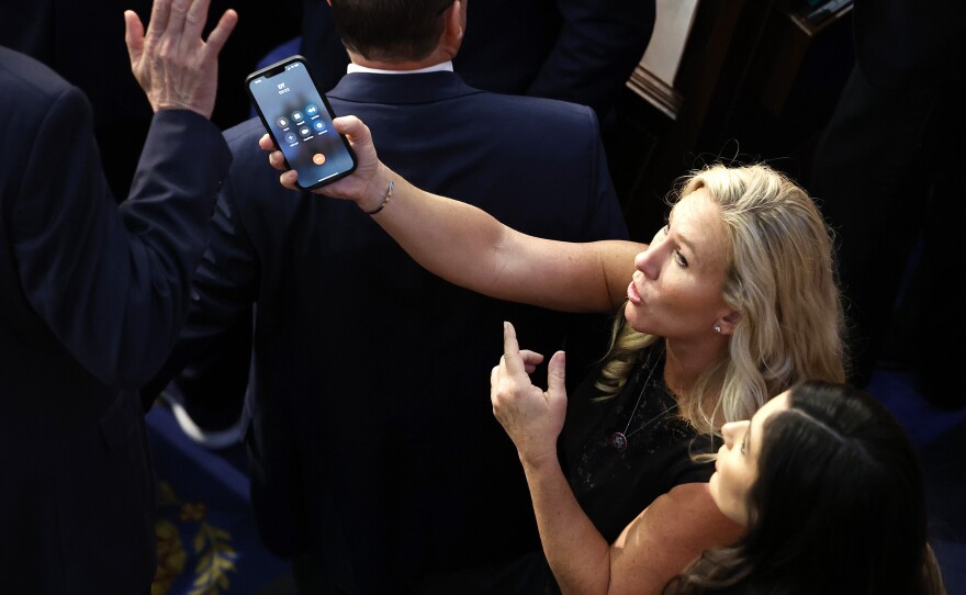Rep.-elect Marjorie Taylor Greene (R-GA) offers a phone with the initials "DT" to Rep.-elect Matt Rosendale (R-MT). It was former President Donald Trump on the line.