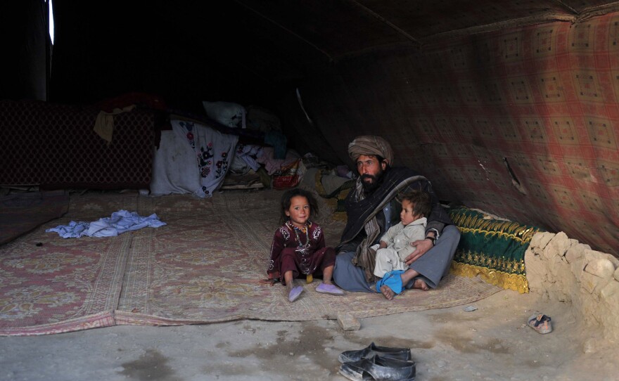An Afghan internal refugee man sits in a tent with two children on the outskirts of Jalalabad.
