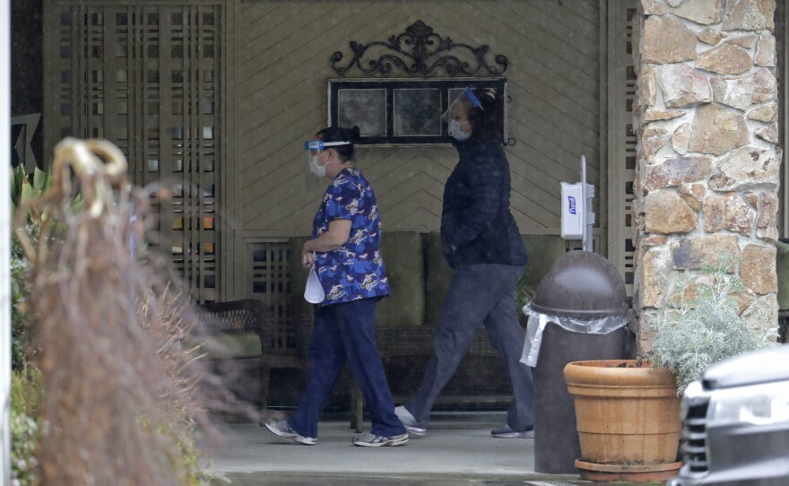 Two workers approach the entrance to Life Care Center in Kirkland, Wash., on March 13. An association that represents nursing homes is asking for billions of dollars in federal relief funds to cope with the coronavirus crisis.