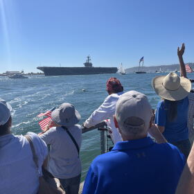 People gather with American flags along Shelter Island's shoreline ahead of the USS Lincoln's arrival, Oct. 8, 2026.