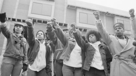 Mourners of MOVE members killed in the 1985 bombing by the Philadelphia police stand in front of their former headquarters. They raise their arms with the Black Power salute during the funeral procession for leader John Africa.