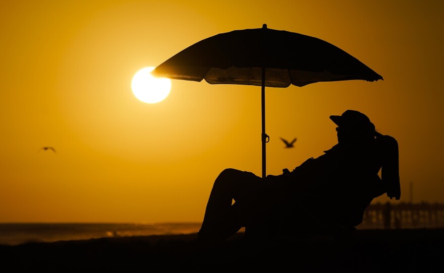 A person rests under an umbrella as the sun sets, Sept. 12, 2023, in Newport Beach, Calif. After a summer of record-smashing heat, warming somehow got even worse in September as Earth set a new mark for how far above normal temperatures were, the European climate agency reported.