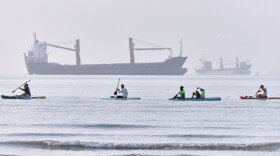 People paddle along the shoreline as cargo ships are anchored in the Strait of Hormuz off Bandar Abbas, Iran, on Monday.