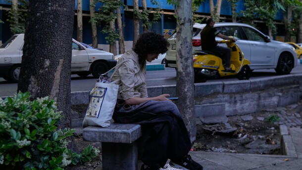 A woman checks her smartphone while sitting on a bench along a sidewalk in northern Tehran, Iran, Tuesday, May 26, 2026.
