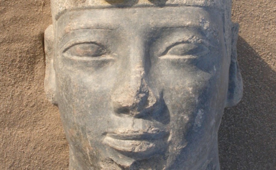 A close-up of the statue of Taharqa surrounded by sand.