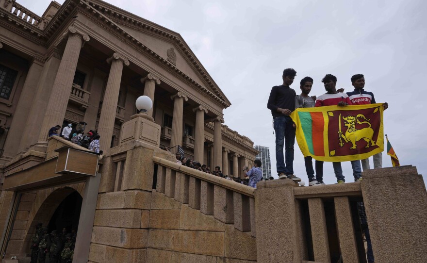 People stand holding a national flag at the President Gotabaya Rajapaksa's office on the second day after it was stormed in Colombo, Sri Lanka, on Monday.