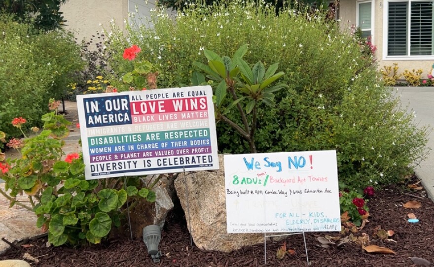 Two yard signs in front of a University City home; one declares "In our America, all people are equal; love wins; Black lives matter; immigrants and refugees are welcome; disabilities are respected; women are in charge of their bodies; people and planet are valued over profit; & diversity is celebrated" while the other says, "We say NO! 8 ADUS / Backyard apt towers" 