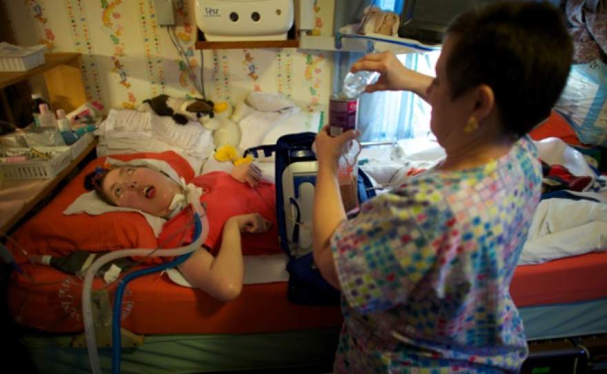 Olivia Welter breathes with the help of the portable ventilator on the back of her wheelchair. She can't speak; she can't move. Her eyes are wide open — she can't even close her eyelids. She has been severely disabled since birth.