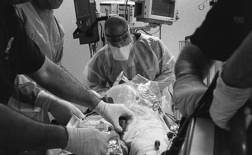 Dr. Brett Barro stands at the head of a COVID-19 patient's bed to speak with him. At home, the patient became rapidly hypoxic (their body lacked adequate oxygen) and now would require intubation for a chance at survival.