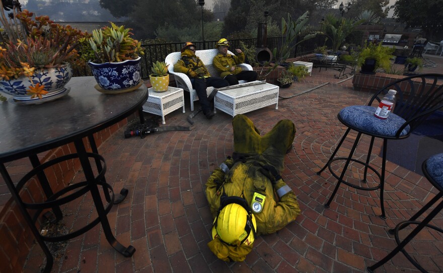 Los Angeles City firefighters Omar Velasquez, center, sleeps as Cory Darrigo, left, and Sam Quan rest in the backyard of home they were protecting after fighting the Woolsey Fire on November 9, 2018 in Westlake Village, Calif.