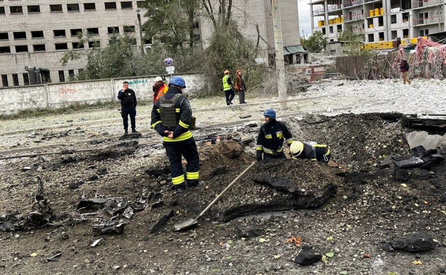Emergency workers clear debris from the crater of a missile strike at a bus stop in a residential area of Dnipro, Ukraine. Missiles struck multiple cities across the country Monday morning.