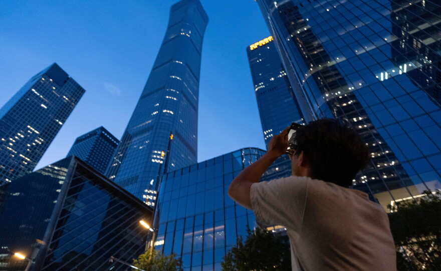 A passerby tries to take photo of the damage on the Citic Tower also known as Zun Tower in Beijing, China, Friday, June 26, 2026.