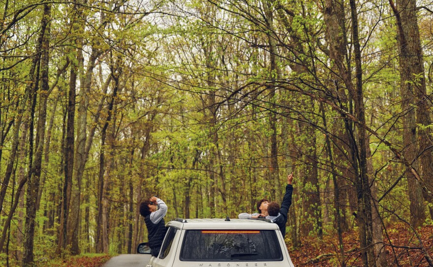 The teammates sit on the ledges of their SUV's rolled-down windows while looking for birds at High Point State Park.