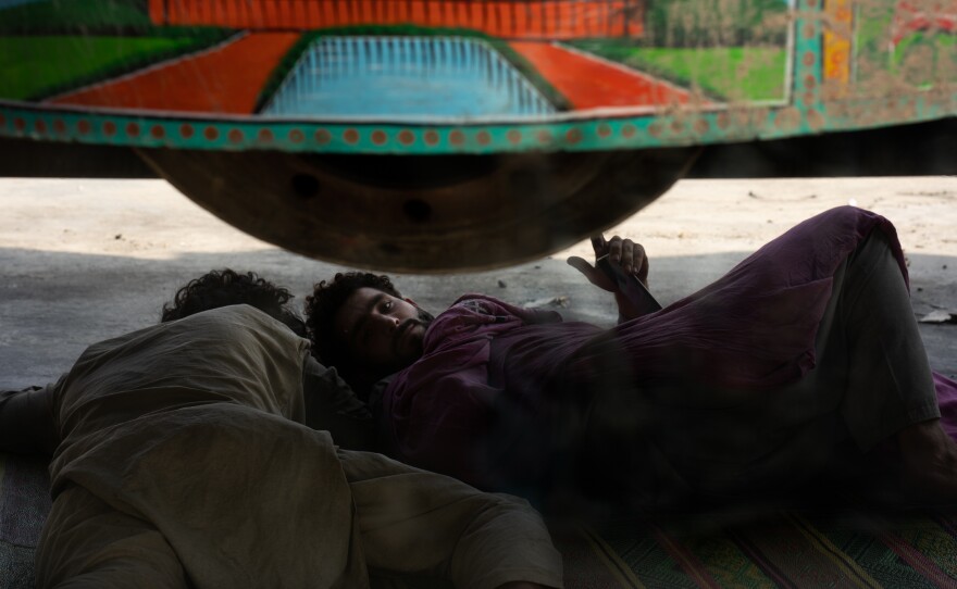 With border traffic at a standstill, men rest under a truck while waiting to get into Afghanistan.