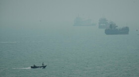 A motorboat travels past commercial vessels anchored amid haze in the Strait of Hormuz off Bandar Abbas, Iran, Monday, Sept. 7, 2026.