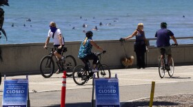 People use the bike path as surfers are seen in the background, Thursday, April 23, 2020, in Ventura, Calif.