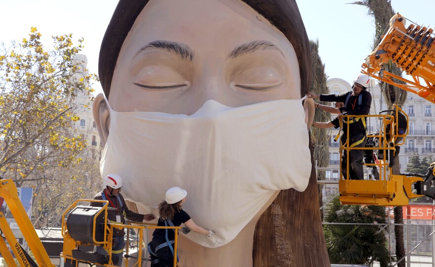 The World Health Organization called the COVID-19 viral disease a pandemic Wednesday. Here, workers in Spain place a medical mask on a figure that was to be part of the Fallas festival in Valencia. The festival has been canceled over the coronavirus outbreak.