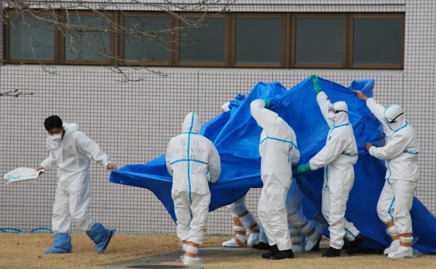 Japan Self-Defence Force officers in radiation protection suits hold a blue sheet over workers who were exposed this week to high levels of radiation at the Fukushima Dai-ichi plant.