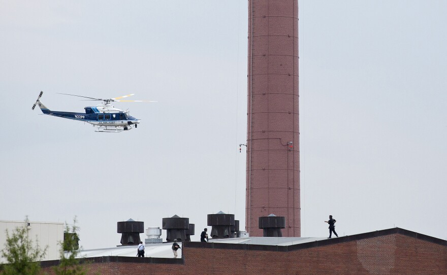 A police helicopter flies overhead as police walk on the roof of a building during the response to the shooting.