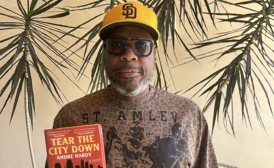 The image is a photograph of author and former NFL player Andre Hardy, as he holds up his novel "Tear the City Down" at KPBS on September 1, 2026.