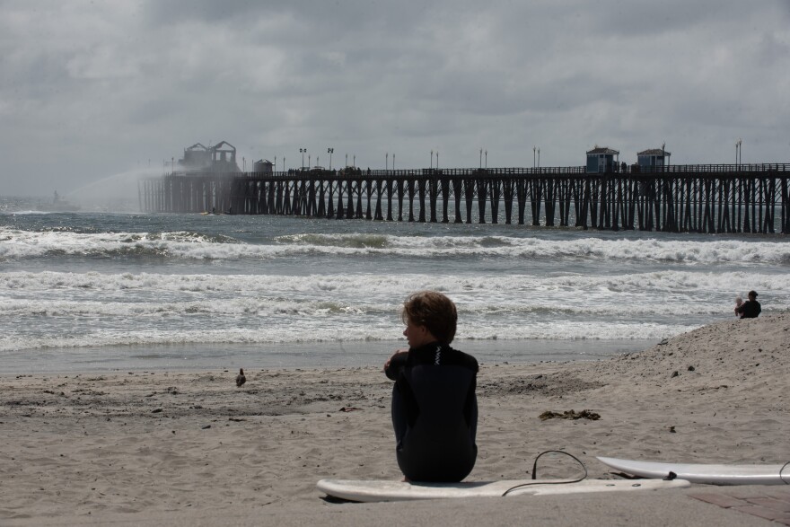 A surfer looks toward the ocean as crews work to contain a fire on the Oceanside Pier, April 26, 2024.