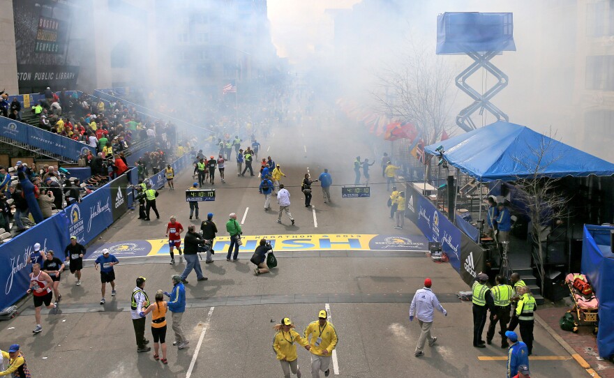 The Boston Marathon finish line moments after two bombs exploded on April 15, 2013. With the race clock reading 4:10:10, Demi Clark can be seen in the bottom left (yellow top, braided hair, black tights) telling two race officials that she had to get to her family in the stands.