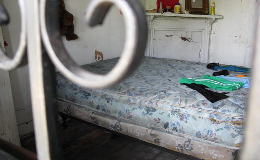 The front room of this deteriorating house has become a bedroom for one squatter. There is no electricity or running water, and there is nowhere to keep fresh food. The squatter uses a bungee cord to keep the door closed at night.
