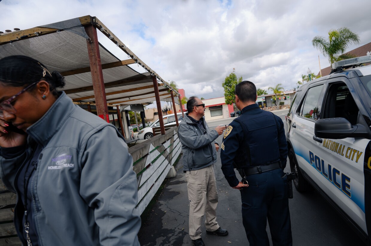 National City HOME team caseworker Qiana Williamson, left, speaks on the phone as Hector Hueso speaks with National City police officer outside a restaurant while responding to a homelessness-related call on March 7, 2024. National City is the second in San Diego County to move away from a police-led response to homelessness and toward trained caseworkers.